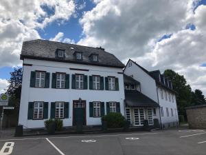 a white building with black shutters on a parking lot at Kloster Steinfeld Gästehaus in Kall