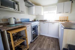 6 Berth Caravan For Hire In Hunstanton At Manor Park Holiday Park Ref 23004a في هونستنتون: مطبخ بدولاب بيضاء وفرن علوي موقد