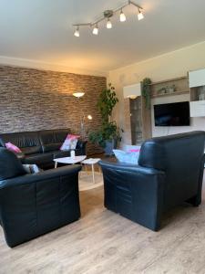 a living room with black leather furniture and a brick wall at Hof Görrespesch-Ferien im Herzen der Schneifel in Schlausenbach