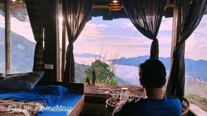 a person sitting in a bed looking out of a window at 1941M Homestay Tà Xùa in Bắc Yên