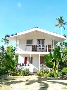 a white house with palm trees in front of it at Bayay ni Nanay Bed & Breakfast in Magpupungko Beach Road in Pilar