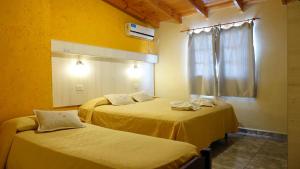 two beds in a room with yellow walls and a window at Aranjuez Real in Villa Carlos Paz