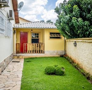 a yellow house with a red door and a yard at Flats Casa de Violeta in Tiradentes