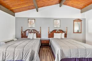 two beds in a room with white walls and wooden ceilings at FairBridge Inn and Suites West Point in Highland Falls