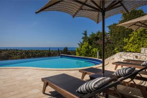 uma piscina com um guarda-sol e cadeiras e uma mesa em Luxury Villa Karmaniolos Fiskardo Kefalonia em Fiskardho