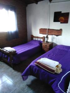 2 bedden in een kamer met paarse lakens bij Cabañas Don Fernando in Santa Rosa de Calamuchita