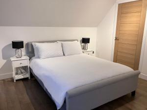 um quarto com uma cama com lençóis brancos e 2 candeeiros em Berryfield Holiday Apartment em Inverness