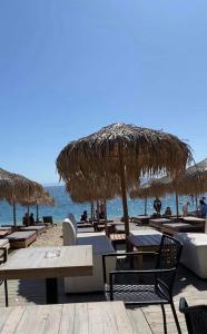 a beach with tables and straw umbrellas and the ocean at Athens Victoria's Apartment in Athens