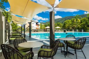 eine Terrasse mit Tischen und Stühlen neben einem Pool in der Unterkunft Belle Escapes Luxury Rainforest Villa Palm Cove in Palm Cove