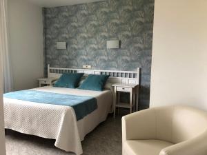 um quarto com uma cama com almofadas azuis e uma cadeira em Hotel Florida em A Lanzada