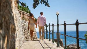 a man and woman walking down a walkway near the ocean at Apartments Villa Dinka in Opatija