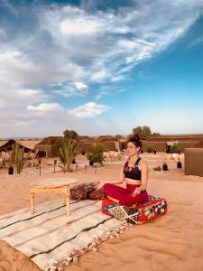 une femme assise sur une planche de surf dans le désert dans l'établissement Sahara wellness camp, à Merzouga