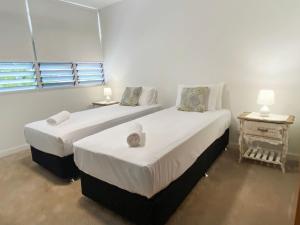 two beds in a white room with two tables at 1 Bright Point Apartment 2303 in Nelly Bay