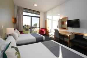 a hotel room with two beds and a desk and a television at Scenic Hotel Punakaiki in Punakaiki