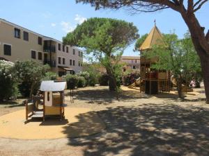 een park met een speeltuin met een gebouw en bomen bij Appartement 5 Couchages tout Confort proche Mer in Le Barcarès