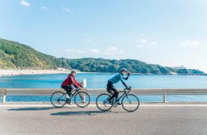 ふるシェアの家すさみ في Susami: شخصان يركبان الدراجات على طريق قريب من المياه