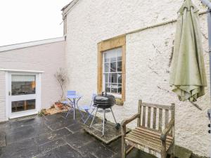 a patio with a grill and a chair and an umbrella at Bower Coach House in Martock