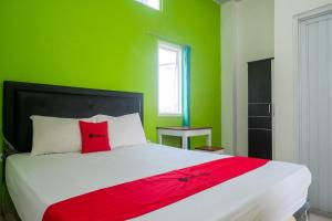 um quarto verde com uma cama branca e uma almofada vermelha em RedDoorz near Pakuwon Mall Solo Baru em Sukoharjo