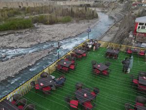 eine Gruppe von Tischen und Stühlen auf einem Feld neben einem Fluss in der Unterkunft Indus Lodges Gilgit in Gilgit