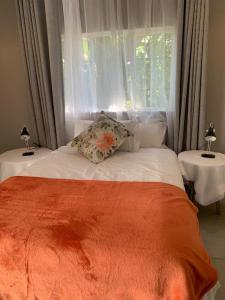 a bed with an orange blanket and a window at KLOOFIES GUESTHOUSE in Roodepoort