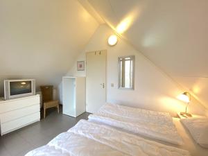 Un dormitorio con una gran cama blanca y un televisor. en Previnaireweg 20, en Callantsoog