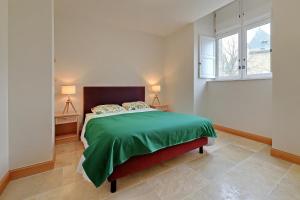 een slaapkamer met een bed met een groen dekbed en 2 ramen bij Petit Marigny - Belle maison pour 10 voyageurs in Alexain