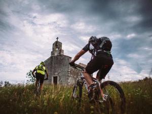 two people riding bikes in a field with an old church at Apartments Hera in Mošćenička Draga