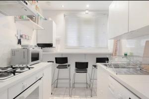 a white kitchen with white counters and stools at The Lovely Room in London