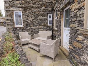 a patio with wicker chairs and a table on a stone wall at Gildabrook Cottage in Bowness-on-Windermere