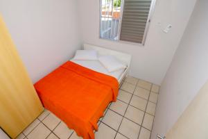Cette petite chambre blanche comprend un lit avec une couverture orange. dans l'établissement Residencial Primavera, à Bombinhas