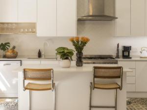 una cocina con armarios blancos y una encimera con 2 sillas en Sweet Orange Guest House, en Ciudad del Cabo