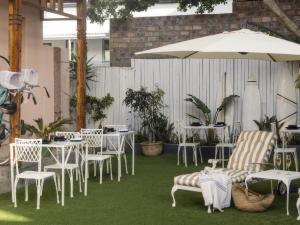 un patio con mesas y sillas blancas y una sombrilla en Sweet Orange Guest House, en Ciudad del Cabo