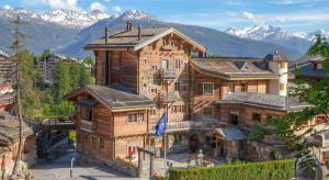 une grande maison en bois avec des montagnes en arrière-plan dans l'établissement Hostellerie du Pas de l'Ours "Relais et Châteaux", à Crans-Montana