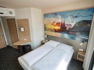 Un dormitorio con una cama blanca y una pintura en la pared en B&B Hotel Köln-City, en Colonia