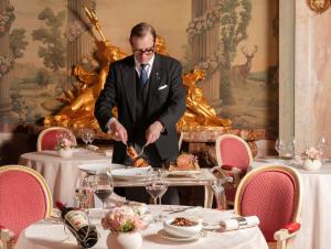 a man in a suit is cutting food on a table at The Ritz London in London