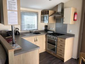 a kitchen with wooden cabinets and a stove top oven at 8 Berth Luxury Caravan With A Full Sea View In Suffolk Ref 20276bs in Hopton on Sea