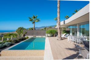 a swimming pool next to a house with palm trees at Los Jardines de Abama Suites in Guía de Isora