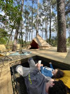 zwei Personen, die vor einem Zelt auf einer Matte liegen in der Unterkunft Tente Indiana Pins - La Téouleyre in Saint-Julien-en-Born