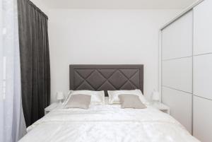 a white bedroom with a large bed with a black headboard at Apartments Tila in Drasnice