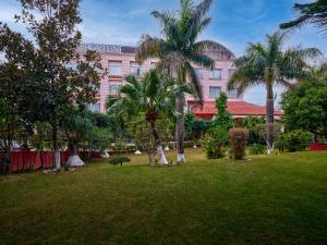 um grande edifício rosa com palmeiras num parque em Fortune Park, Katra - Member ITC's Hotel Group em Katra