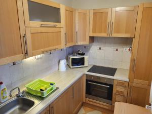 a kitchen with wooden cabinets and a sink and a microwave at Jókai Apartman Szarvas in Szarvas