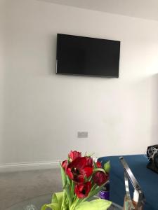 a vase of roses on a table with a tv on the wall at Ainslie Loft in Chingford, London in Chingford