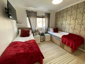two beds in a room with red sheets and a window at Stylish 4 Bedroom House with Private Parking and Free WiFi in Milton Keynes by HP Accommodation in Milton Keynes
