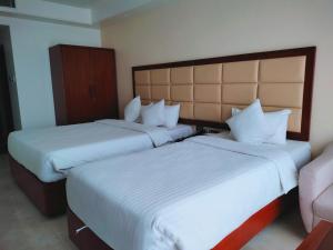 two beds in a hotel room with white sheets at DESHA TARC in Kushtia