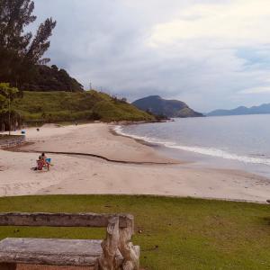 a beach with two people sitting on the sand at Apartamento Reserva do Sahy - Condomínio Aldeia dos Reis in Mangaratiba +19 photos