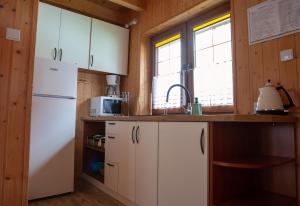 La cuisine est équipée de placards blancs et d'un réfrigérateur blanc. dans l'établissement Bursztynowy Zakątek, à Grzybowo