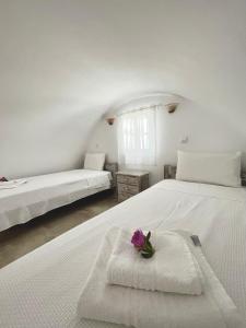 una camera da letto con due letti con lenzuola bianche e un fiore viola di Alonistra Oia Houses a Oia
