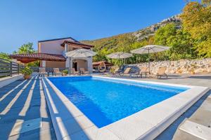 a pool with chairs and umbrellas next to a house at Villa ARIA VALLIS in Tribalj