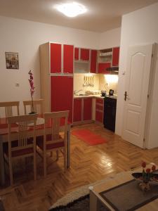 una cucina con armadi rossi, tavolo e sedie di DORA Apartman a Palić