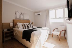 1 dormitorio blanco con 1 cama y 1 silla en Açores Premium- 5 Minutos do Moinhos de Vento, en Porto Alegre